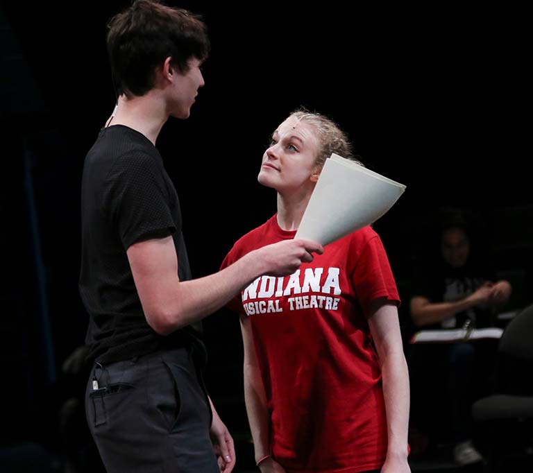 Male and female students rehearsing with scripts.